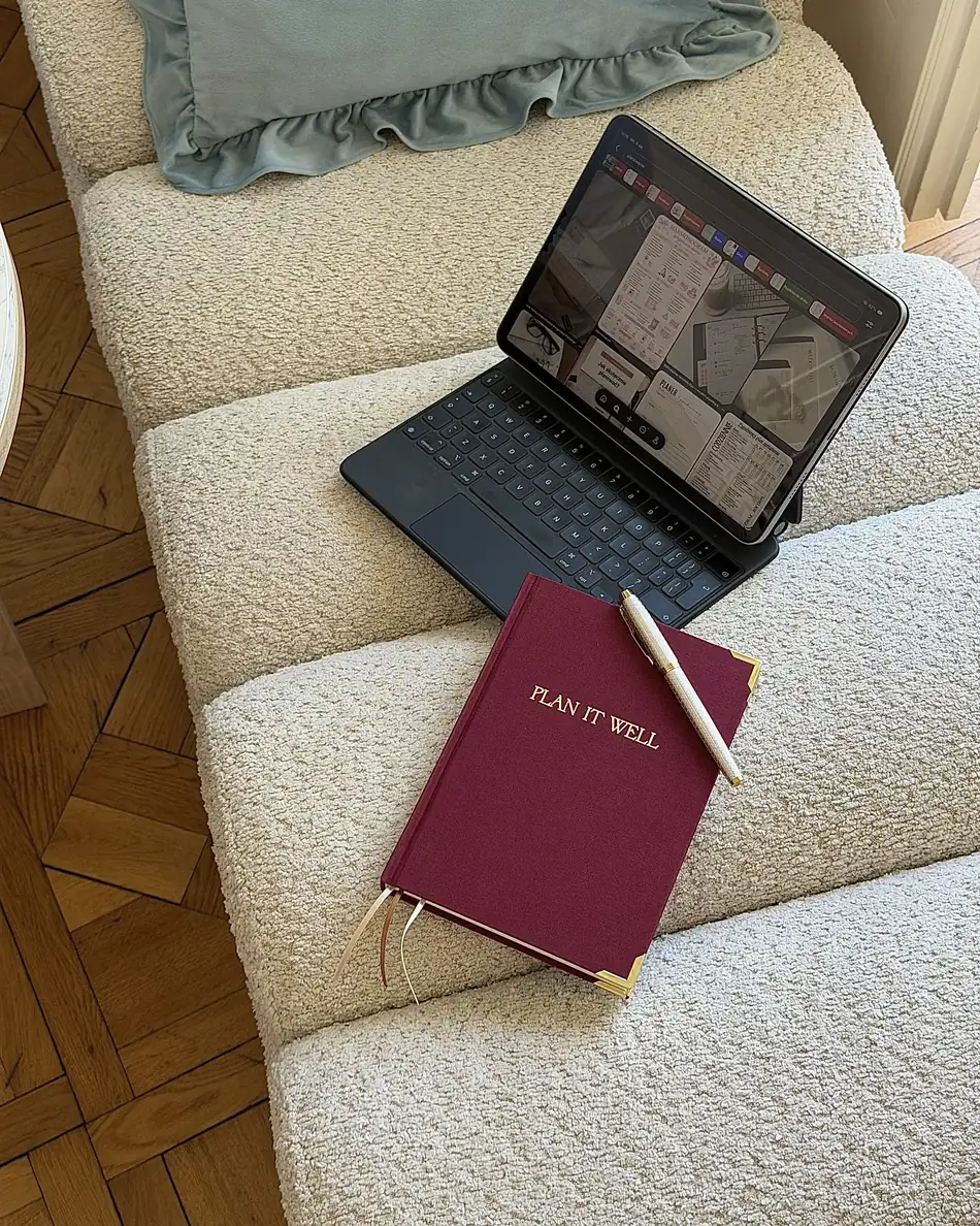 Bordowy planer Plan It Well z długopisem, obok tabletu na fotelu