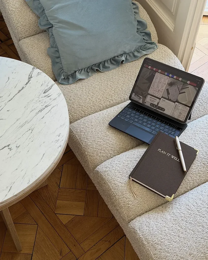 Brązowy planer Plan It Well z długopisem na fotelu z tkaniny boucle, obok tablet