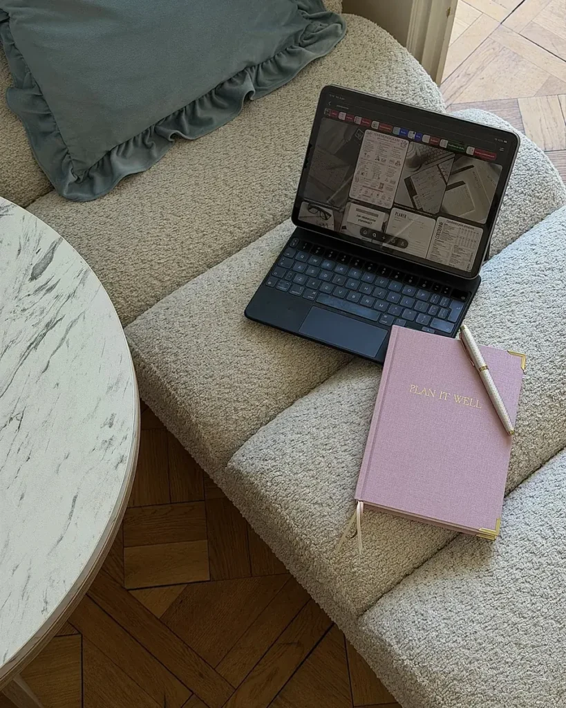 Różowy planer Plan It Well z długopisem na fotelu z tkaniny boucle, obok tablet